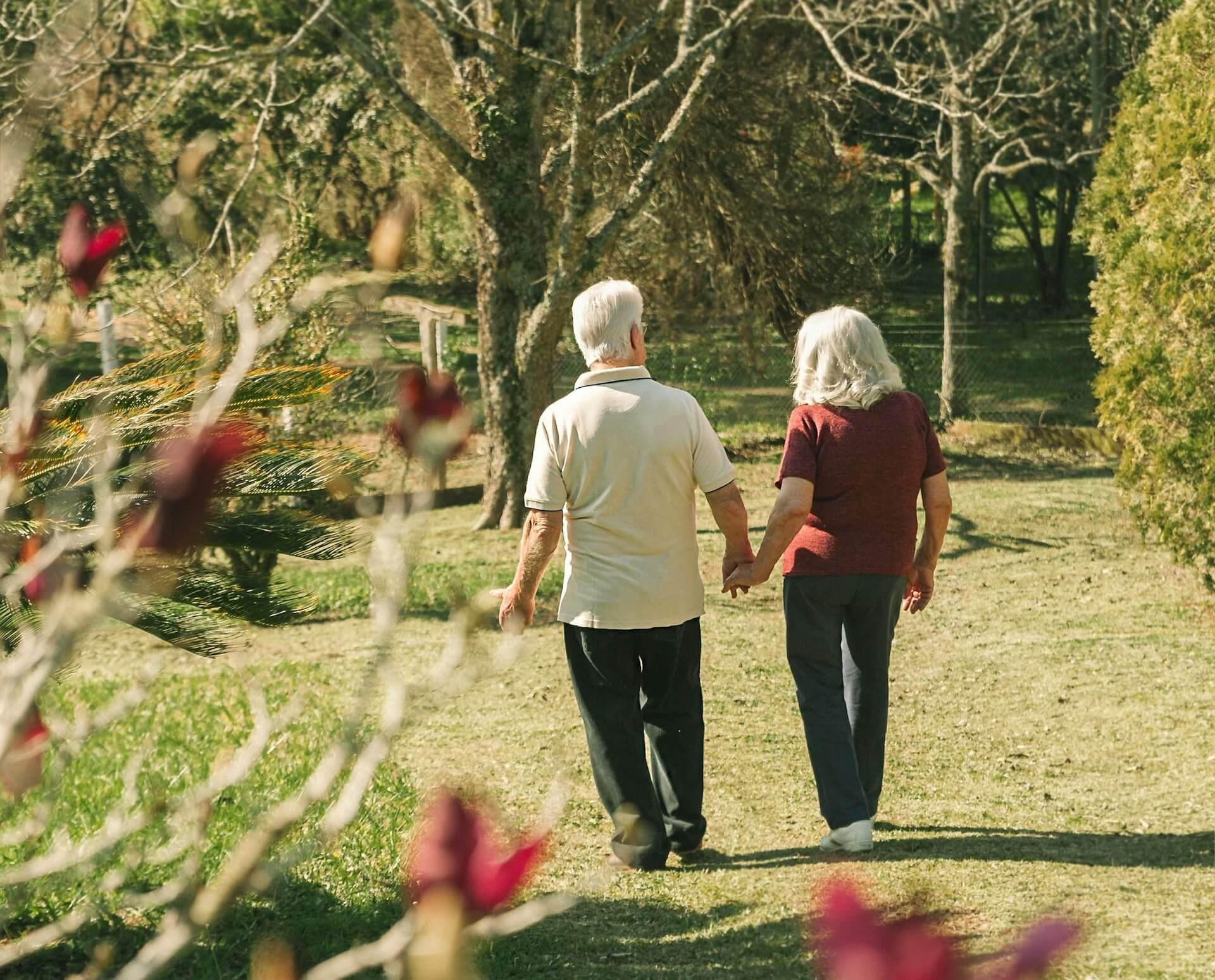 An elderly couple walking hand in hand in a garden